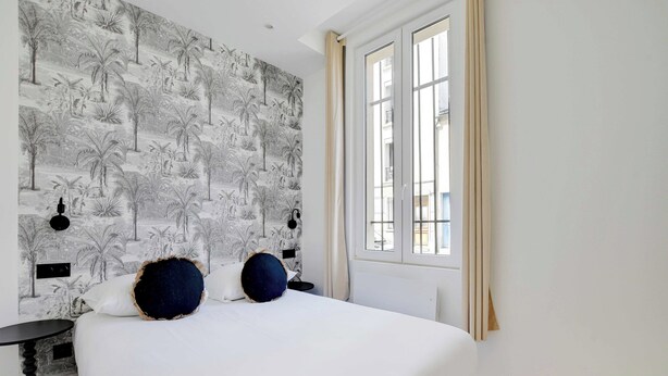 A bedroom with a large bed, a patterned wallpaper, a window with curtains, and a small table.