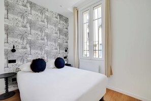 A bedroom with a large bed, a patterned wallpaper, a window with curtains, and a small table. - Cosy Apartment - 2BR - 4P - Montreuil (Montreuil)