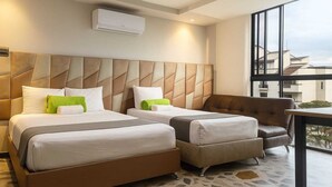 A hotel room with two beds, a sofa, a small table, and a large window offering a view of buildings. - HOTEL AIRPORT PEREIRA (Pereira)