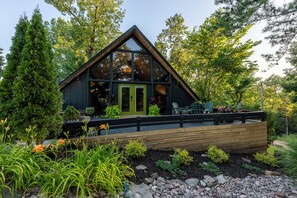 Eine moderne Holzhütte mit einer Holzterrasse, umgeben von üppiger Vegetation und Bäumen.