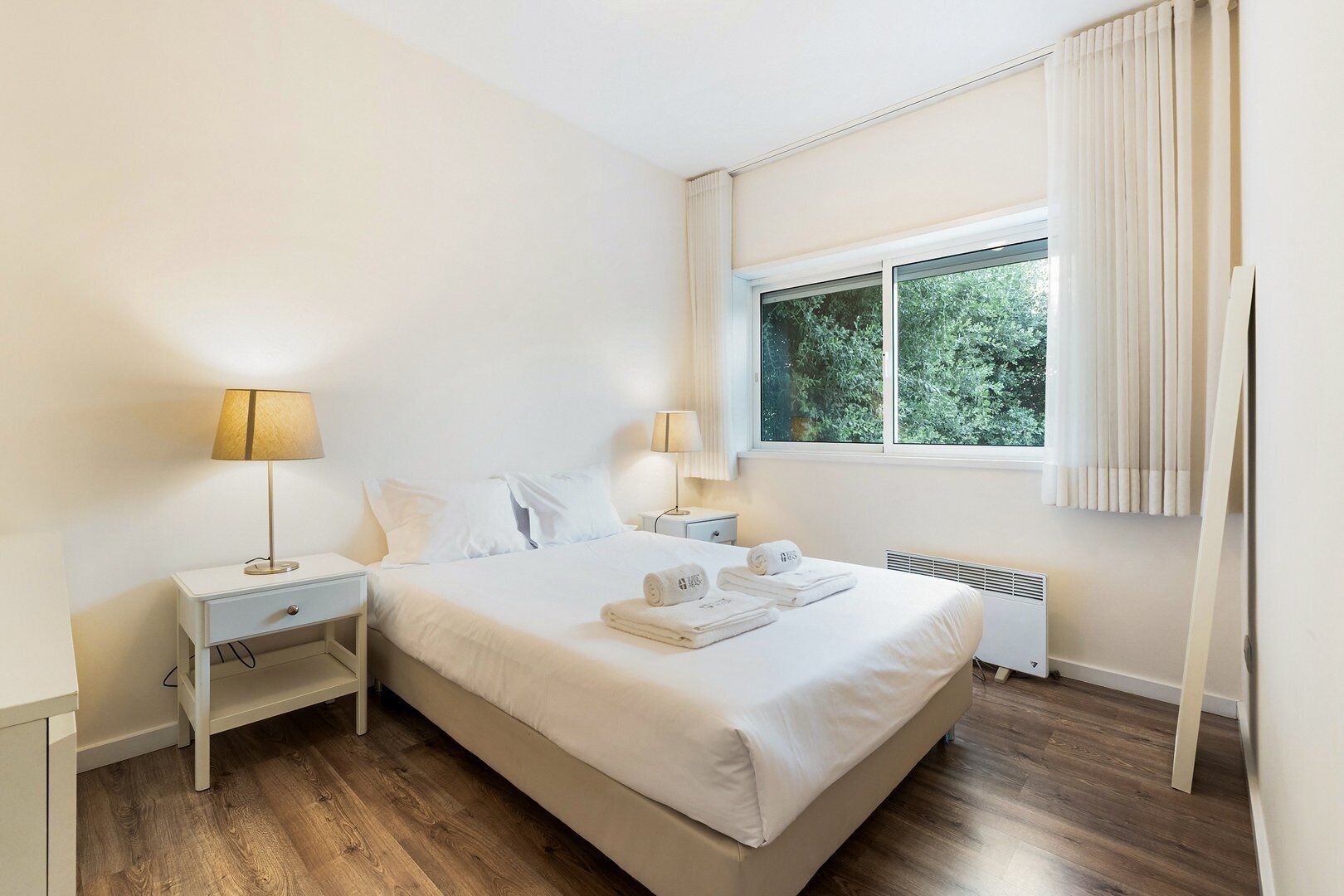 Une chambre d’hôtel avec un grand lit, deux tables de chevet, une fenêtre avec des rideaux et un radiateur.