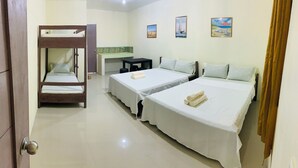 A hotel room with two single beds, a bunk bed, a desk, and a small kitchenette.