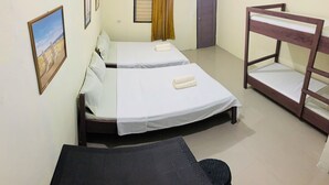 A room with two single beds, a bunk bed, a small table, and a window with a curtain.