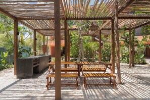 An outdoor seating area with wooden benches and tables, surrounded by a pergola structure. - 3-Bedroom Condo in Aldea Savia (Tulum)