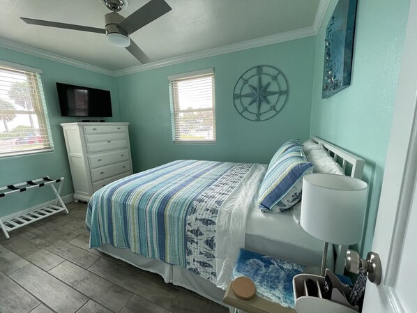 A bedroom with a bed, a dresser, a TV, a ceiling fan, a window, and a wall clock.