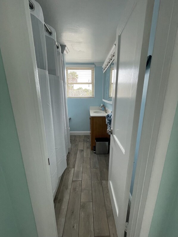 A narrow hallway with a bathroom featuring a sink, mirror, and window.