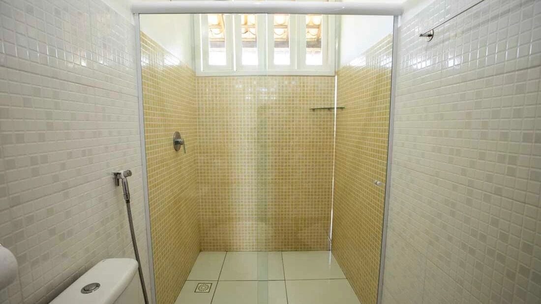 A small, enclosed shower area with tiled walls and floor, a glass door, and a window above.