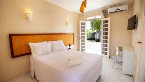 A hotel room with a large bed, a desk, and an open door leading to a balcony. - Pousada Aruana Praia (Aracaju)
