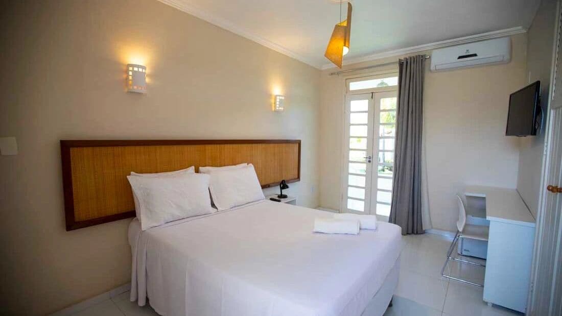 Una habitación de hotel con una cama grande, dos lámparas de noche, un televisor de pantalla plana y un ventanal con cortinas.