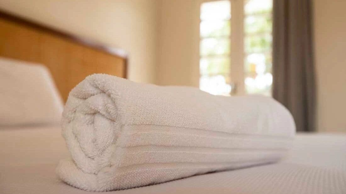 Een keurig gevouwen witte handdoek op een bed met een houten hoofdeinde.