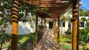 A covered walkway with wooden pillars, leading to a building with white walls and a door. - Pousada Aruana Praia (Aracaju)