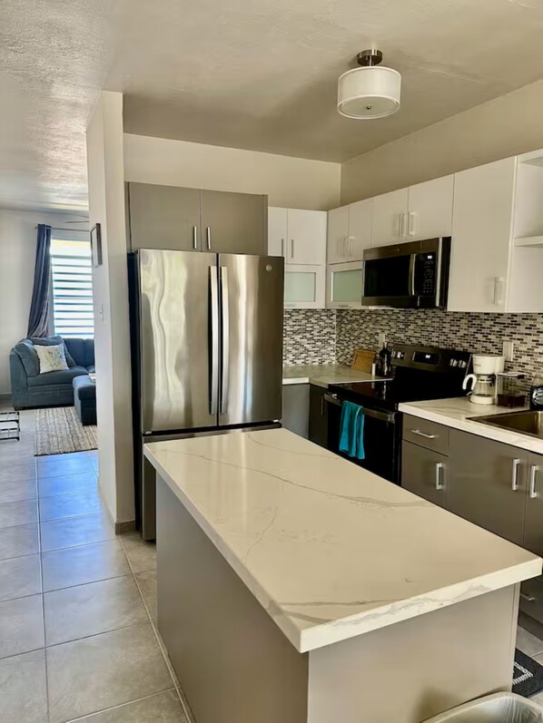 A modern kitchen with stainless steel appliances, a central island, and a dining area with a grey sofa.