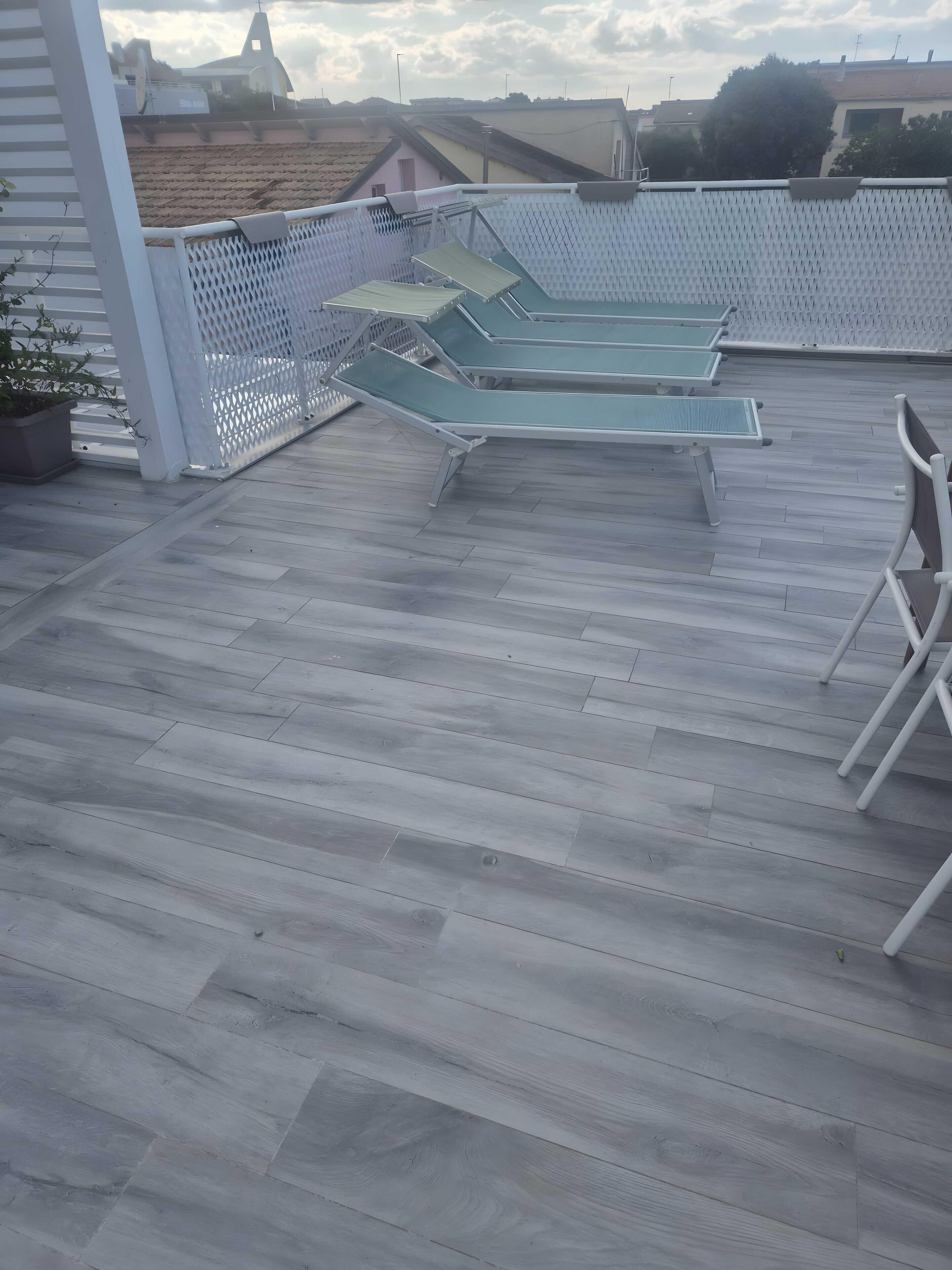 Eine Dachterrasse mit drei Liegestühlen und einem weißen Zaun.