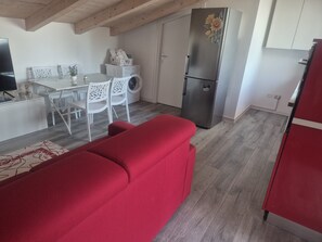 A compact kitchen with a washing machine, a dining area with white chairs, and a red sofa.
