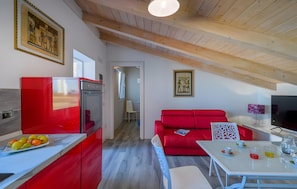 A modern kitchen with a red refrigerator, a dining area with a red sofa, and a TV on a white table.
