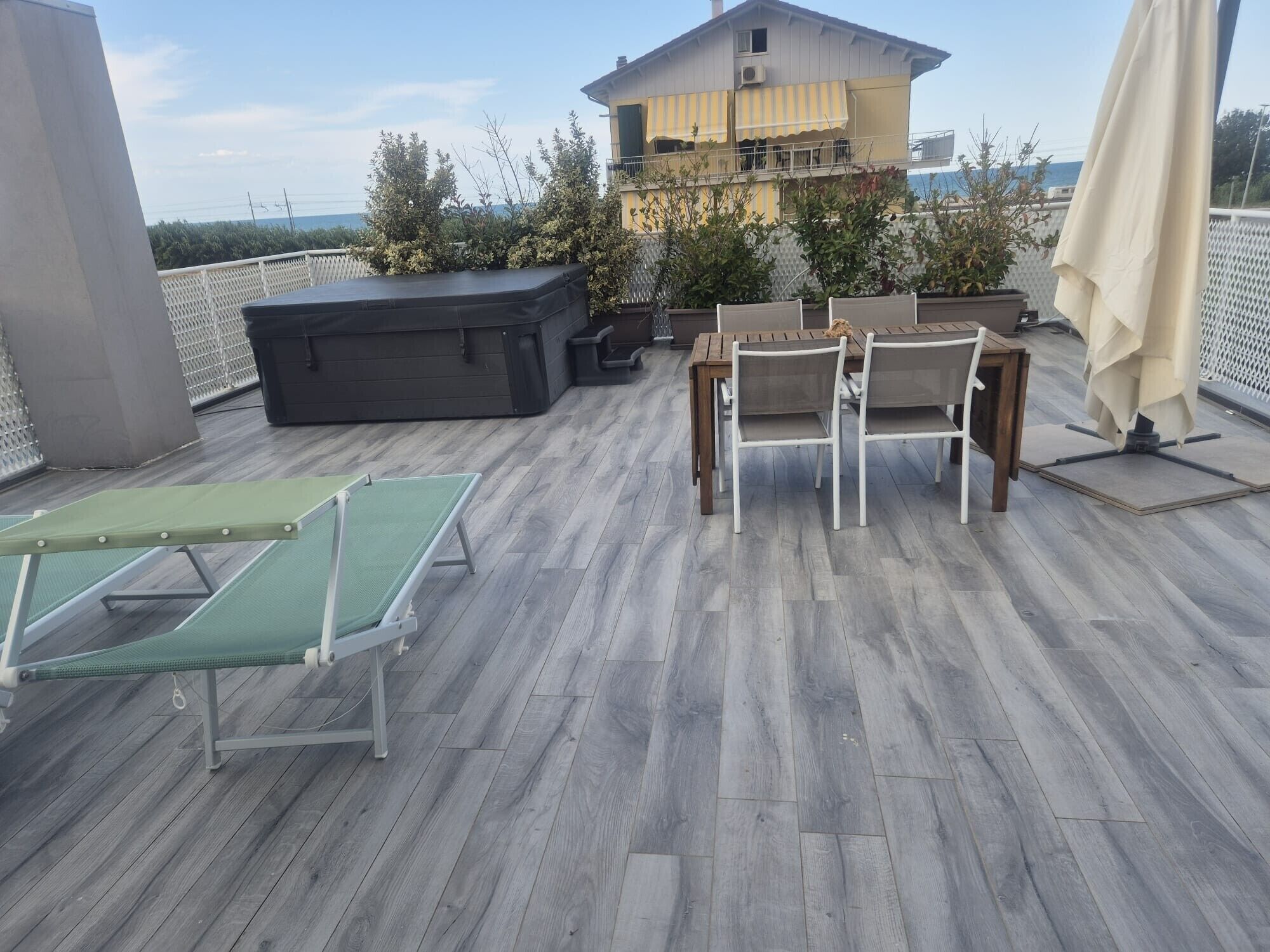 Eine Dachterrasse mit Tisch und Stühlen, einer Liege und Blick auf ein Gebäude.