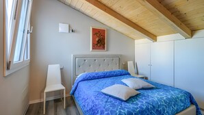 Un dormitorio con cama, una silla, un armario y un cuadro en la pared.