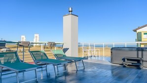 Una terraza con sillones, un jacuzzi y una baranda con vista al agua.