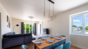 Un comedor moderno con una mesa de madera dispuesta para seis personas, sillas azules y un sofá oscuro al fondo.