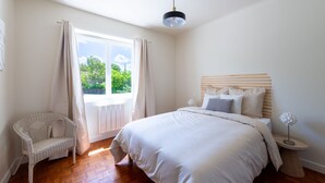 Un dormitorio con una cama grande, una silla, una mesita de noche y una ventana con cortinas.