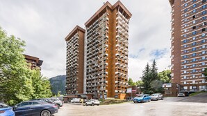 Un parking contenant plusieurs voitures, entouré d’immeubles résidentiels à étages élevés dotés de balcons.