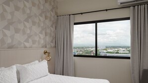 Una habitación de hotel con cama, una silla, ventana con cortinas y pared con diseño geométrico.
