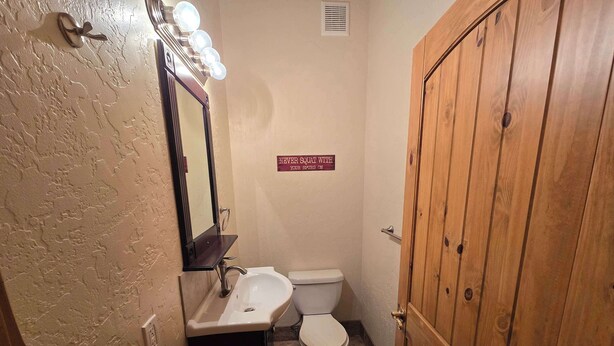 A bathroom with a sink, mirror, and toilet. There is a wooden door and a sign on the wall. - Therriault Pass Sanctuary 6ppl (Eureka)