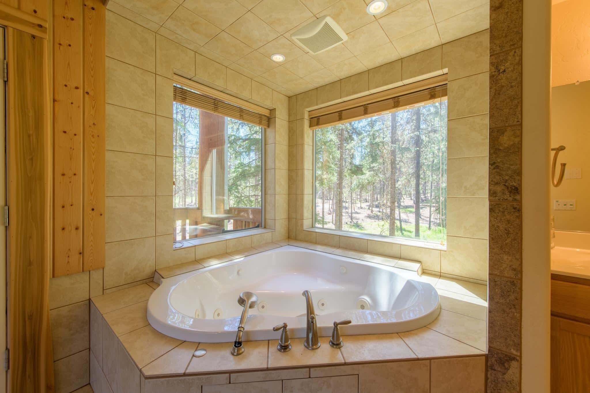 A large, freestanding bathtub in a modern bathroom with large windows and a view of a forest.