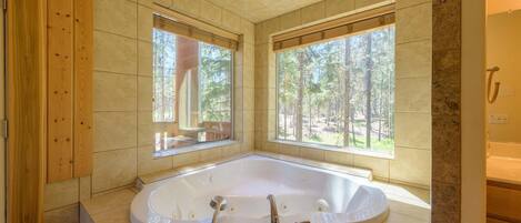 A large, freestanding bathtub in a modern bathroom with large windows and a view of a forest.