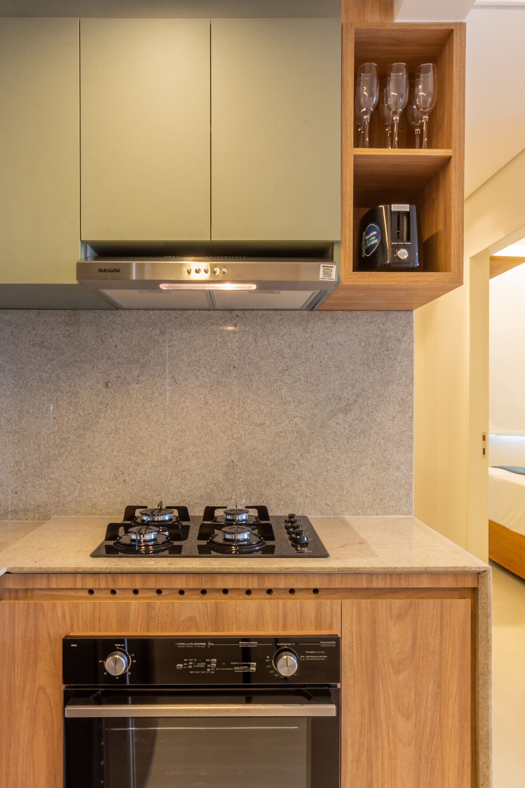A kitchen with a gas stove, oven, and a wooden shelf above containing wine glasses and a microwave.