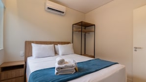 Un letto rifatto con un copergiaccio blu, cuscini bianchi e asciugamani arrotolati su un comodino in legno.
