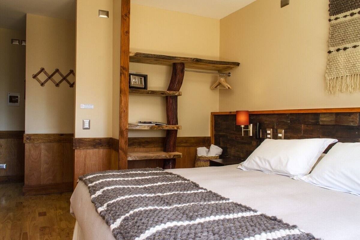 Une chambre à coucher avec une tête de lit en bois, une couverture à rayures et une  étagère en bois sur laquelle est posé un cadre photo.