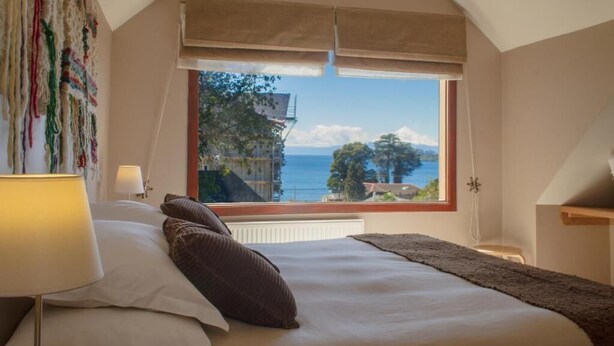 Une chambre avec une grande fenêtre, un lit avec des oreillers, une lampe de chevet et une vue sur la mer.