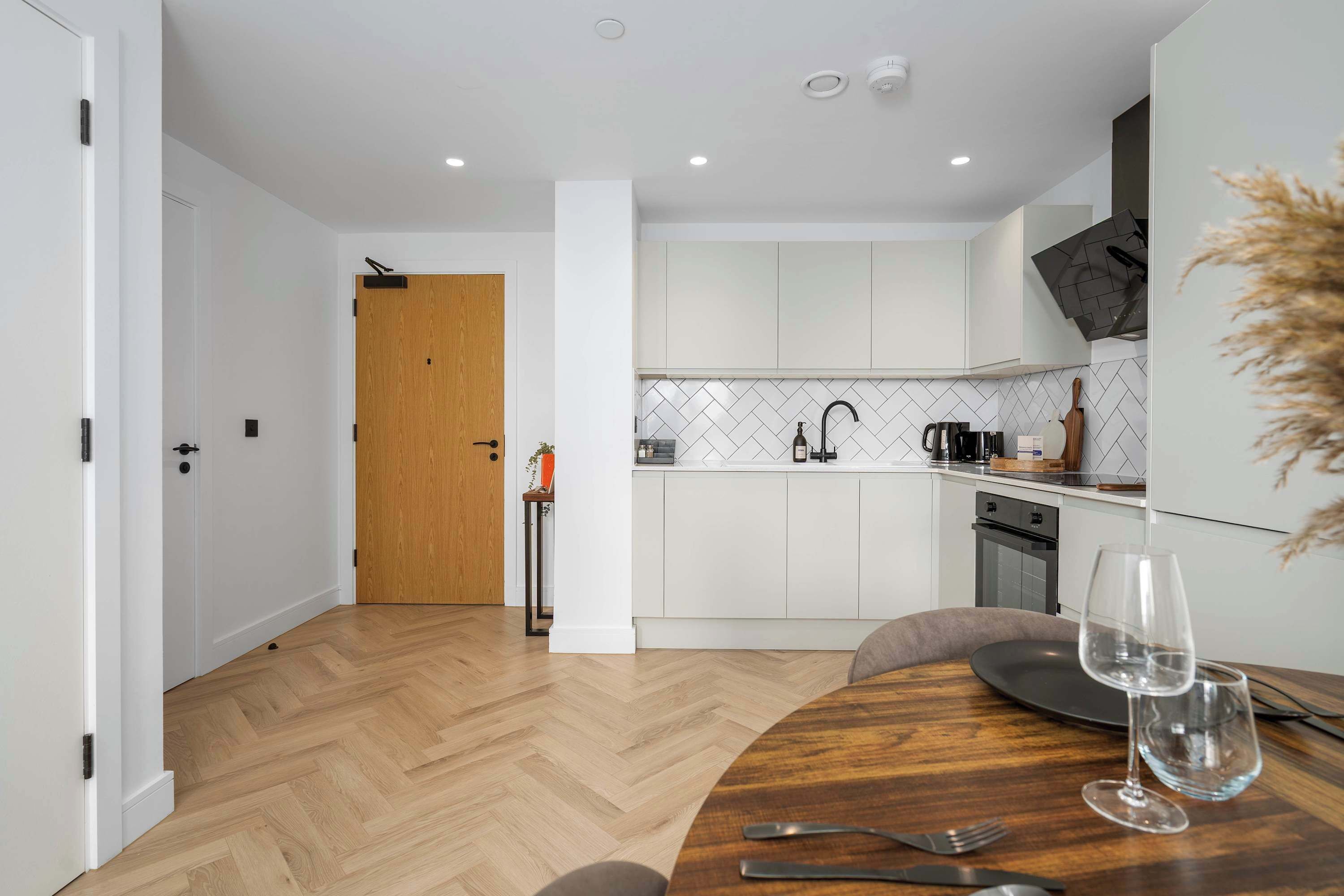 A modern kitchen with white cabinets, a wooden door, and a dining area with a round table and chairs.