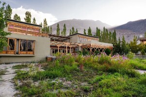 Un edificio moderno con estructura de madera en primer plano, rodeado de un jardín con diversas plantas y flores.