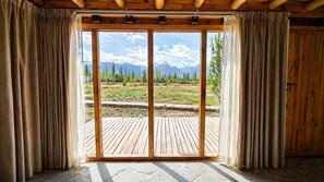 A room with a large sliding glass door leading to an outdoor deck with a mountain view. - Nubra Ecolodge (Leh)