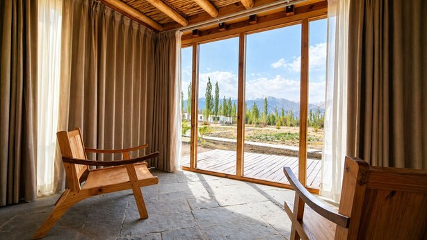 A room with a wooden ceiling, large windows, and a view of a mountainous landscape. - Nubra Ecolodge (Leh)