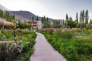 Un sendero conduce a un edificio rodeado de abundante vegetación y montañas.