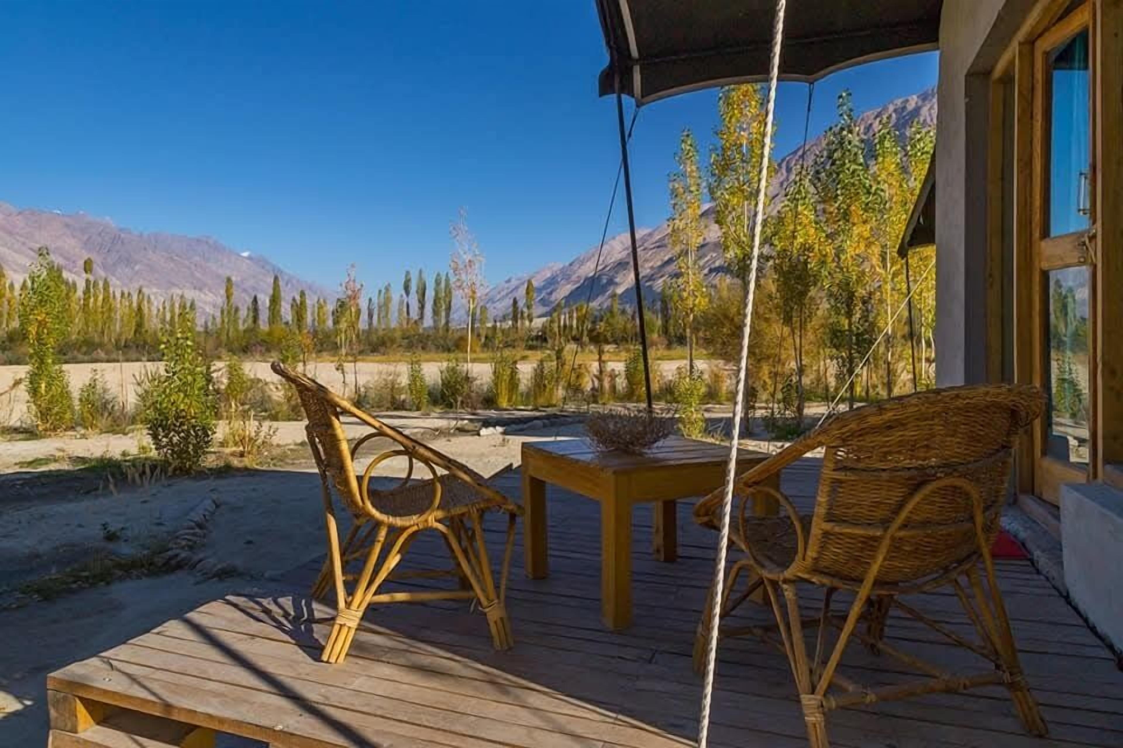 A wooden deck with wicker chairs and a table, overlooking a mountainous landscape.