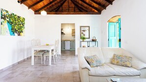 A spacious living area with a high wooden ceiling, a dining table with chairs, a white sofa with floral cushions, and a kitchen in the background. - Home2Book Rural House with Private Pool & BBQ (El Rosario)