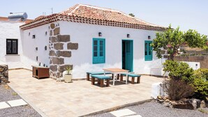 A white building with a tiled roof, stone walls, and a wooden bench area with a table. - Home2Book Rural House with Private Pool & BBQ (El Rosario)