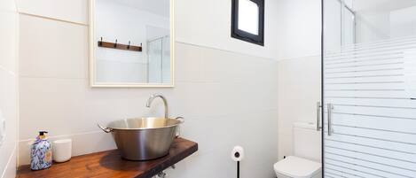 A bathroom with a wooden vanity, a stainless steel sink, a mirror, a toilet, and a glass shower enclosure.