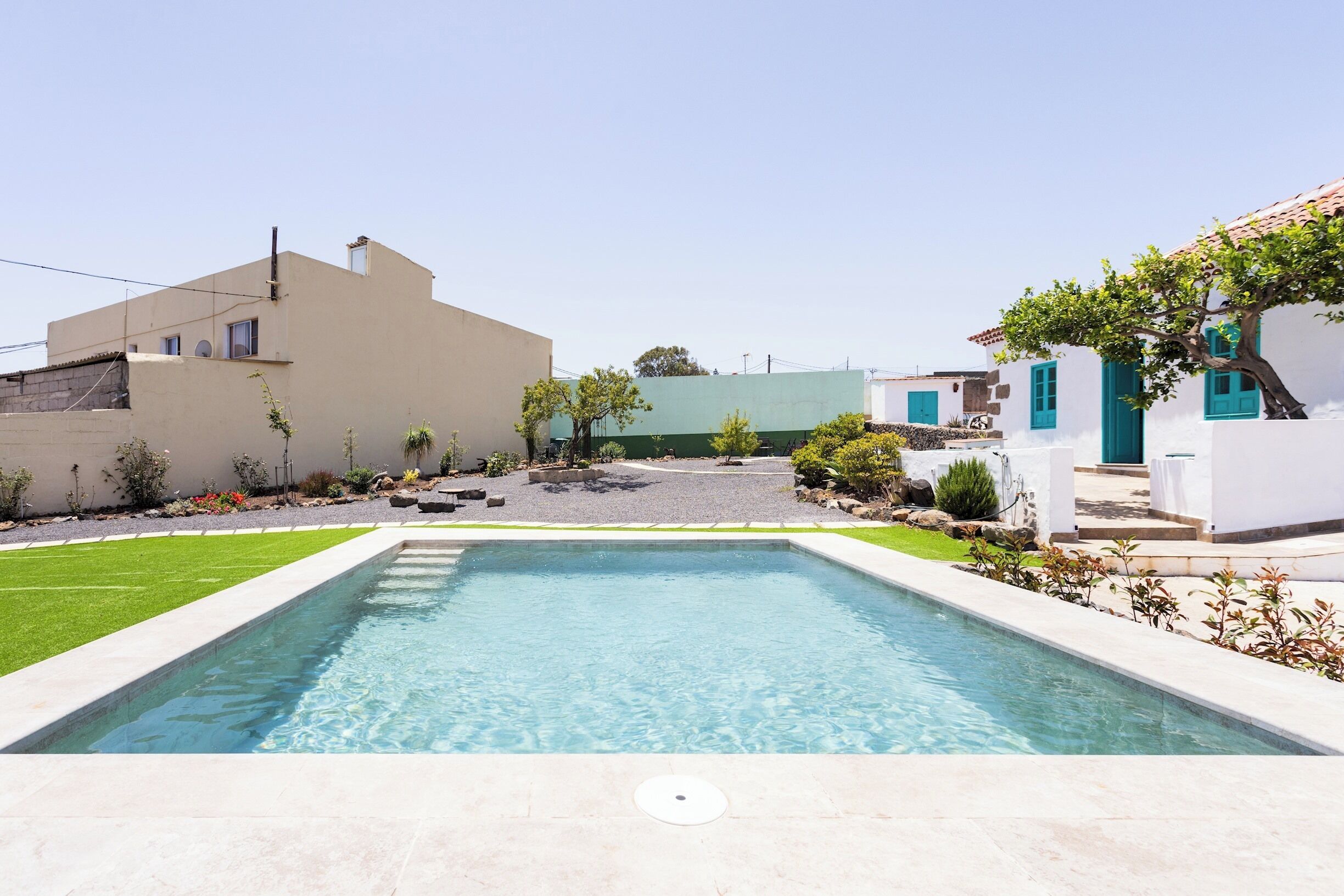 A rectangular swimming pool with a clear blue water surface, surrounded by a well-maintained lawn and a paved area.