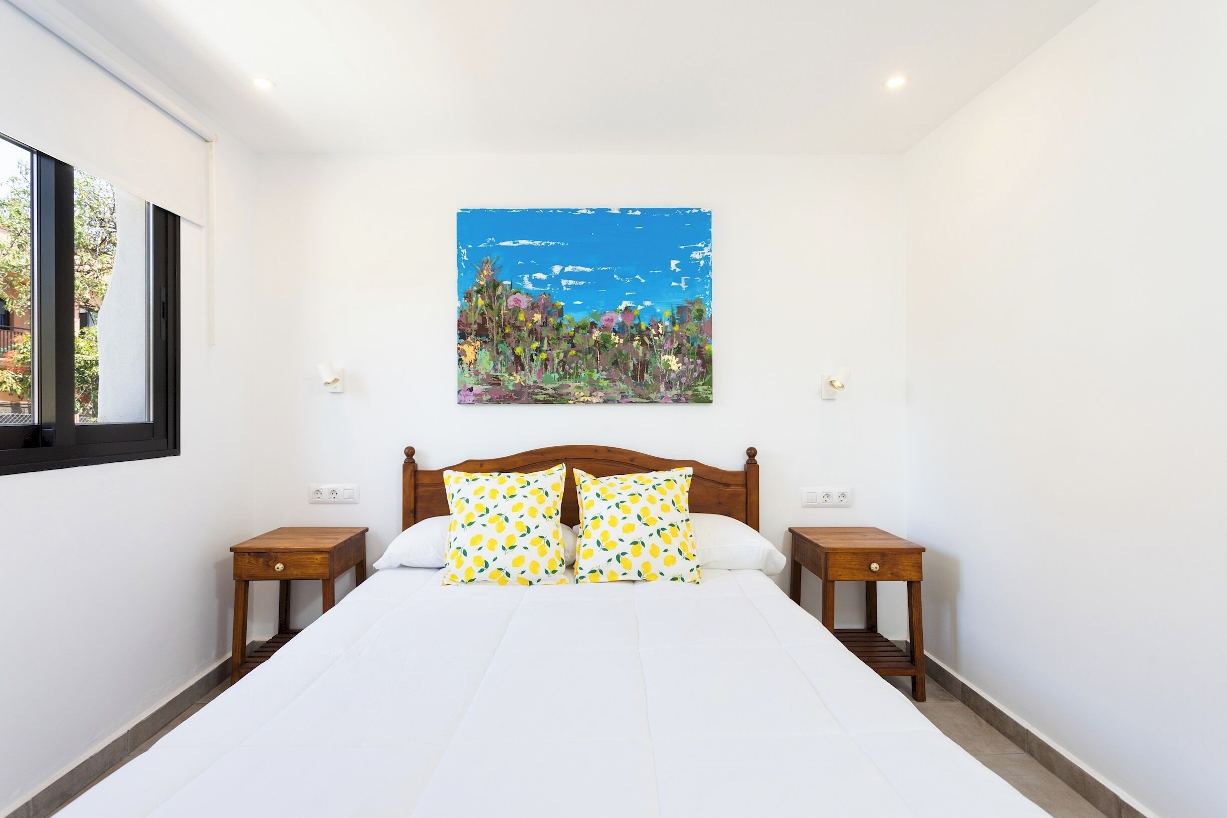 A bedroom with a large bed, wooden headboard, two bedside tables, and a wall-mounted painting of a landscape.