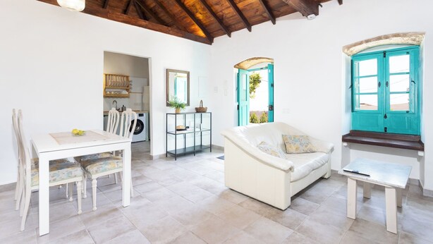 A spacious living area with a white sofa, a dining table with chairs, and a window with a turquoise frame. - Home2Book Rural House with Private Pool & BBQ (El Rosario)