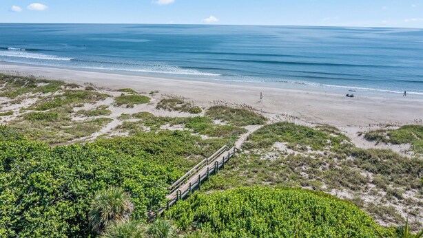 A beach with a wooden walkway leading to the shore, surrounded by greenery and sand. - Walk to Beach, 2 Master Beds, Newly Renovated, Walk to Restaurants, Sleeps 8 (Cocoa Beach)