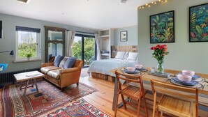 Une chambre confortable avec un grand lit, un coin salon avec un canapé et une table, et un coin repas avec des chaises et une table dressée pour deux personnes.