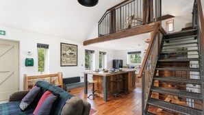 A spacious living area with a wooden staircase, a dining area with a bar, and a cozy seating area with a plaid blanket.