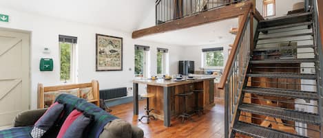 A spacious living area with a wooden staircase, a dining area with a bar, and a cozy seating area with a plaid blanket.