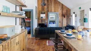 A cozy kitchen with wooden accents, a dining area with a table set for breakfast, and a living area with a sofa and a television.